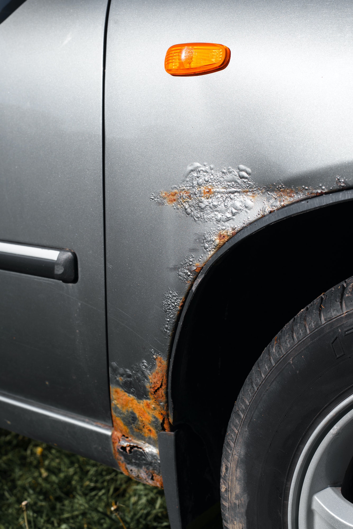 Corrosion of the car. Rust, corroded gray paint on the front fender of the car. Vertical photo
